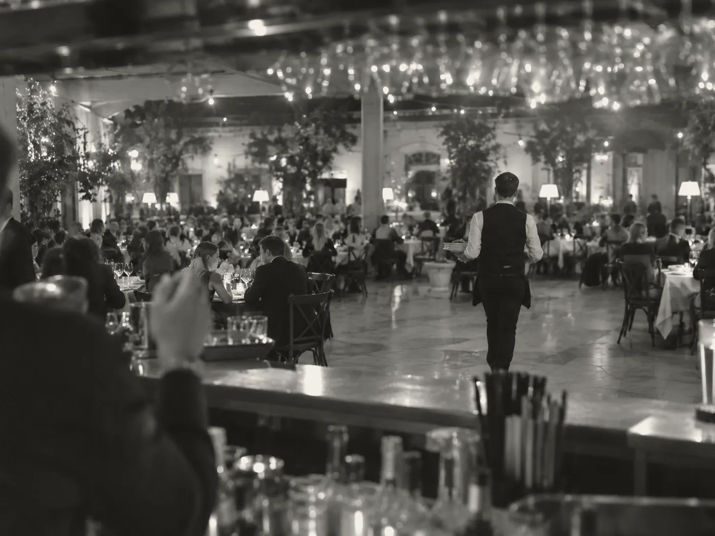 Duża sala restauracji wieczorem widziana zza baru, kelner daleko między stolikami